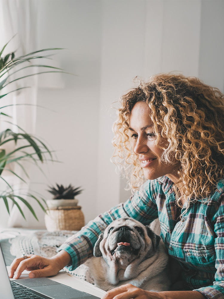 A woman smiling while on the computer with an elderly dog in her lap