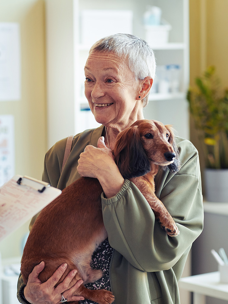 An elderly woman smiling while holding her elderly dog